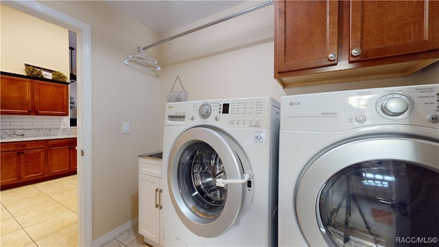 clothes washing area with washing machine and clothes dryer, light tile patterned floors, and cabinets