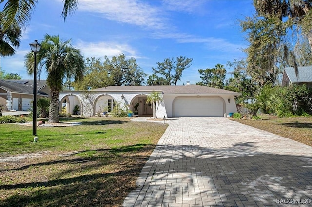 view of front of home with decorative driveway, an attached garage, stucco siding, and a front yard