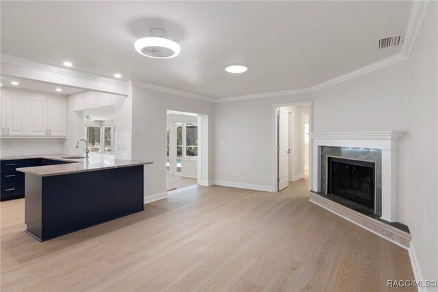 kitchen with light wood finished floors, visible vents, open floor plan, white cabinetry, and a sink