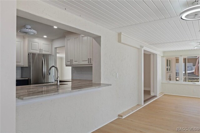 kitchen with stainless steel fridge, a textured wall, light wood finished floors, and light stone countertops