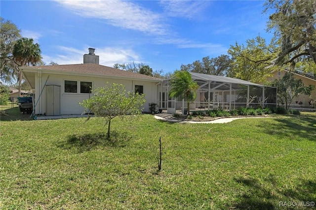 rear view of property featuring a yard, a chimney, a lanai, and stucco siding