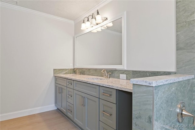 bathroom with a sink, wood finished floors, baseboards, double vanity, and crown molding