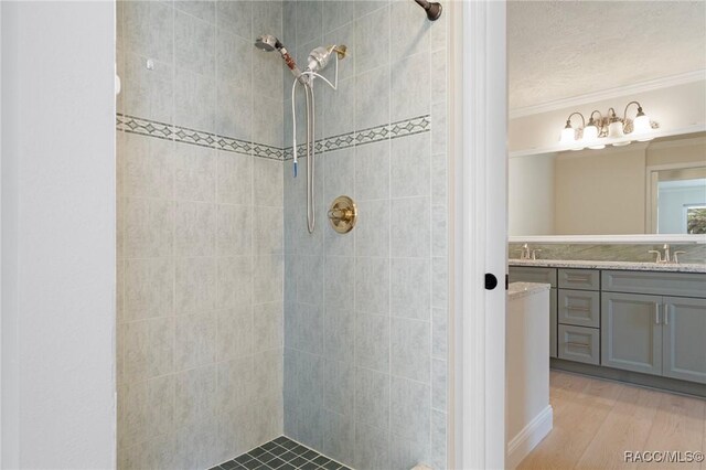 full bath with wood finished floors, a tile shower, vanity, and crown molding