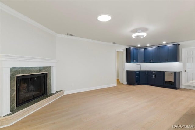 unfurnished living room featuring light wood finished floors, baseboards, visible vents, a premium fireplace, and ornamental molding