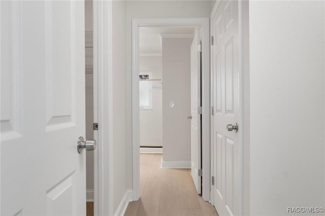 hallway featuring baseboards, baseboard heating, light wood-style flooring, and crown molding