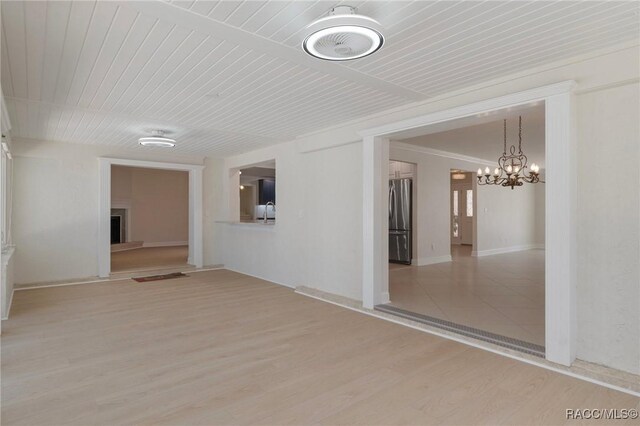 spare room featuring wood ceiling, a fireplace, light wood finished floors, and an inviting chandelier