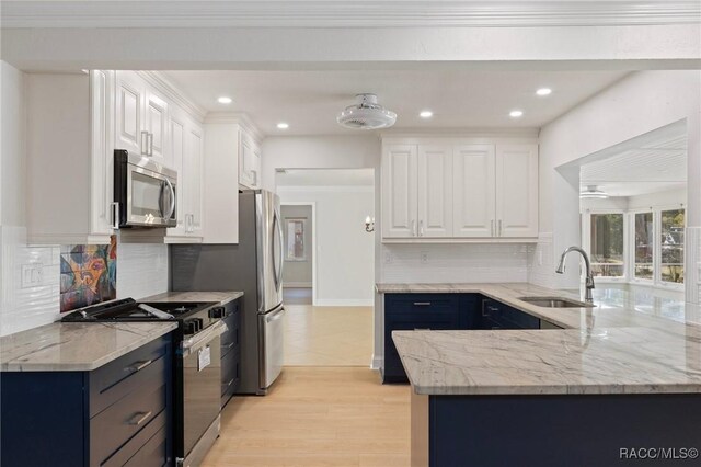 kitchen featuring light stone counters, stainless steel appliances, crown molding, white cabinetry, and a sink