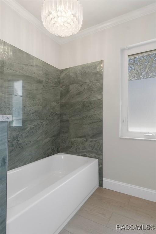 full bath with an inviting chandelier, a washtub, baseboards, and crown molding