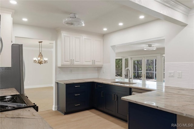 kitchen featuring light stone counters, tasteful backsplash, freestanding refrigerator, white cabinetry, and a sink