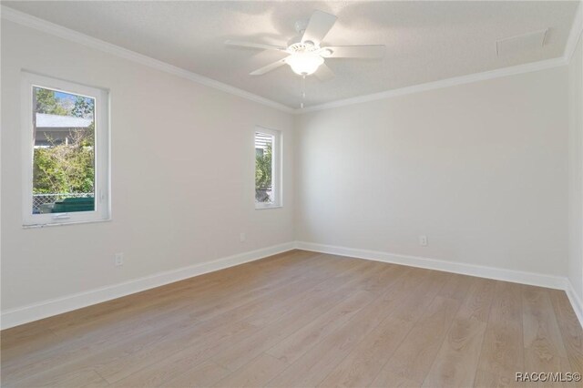 empty room featuring ornamental molding, a ceiling fan, light wood-style flooring, and baseboards