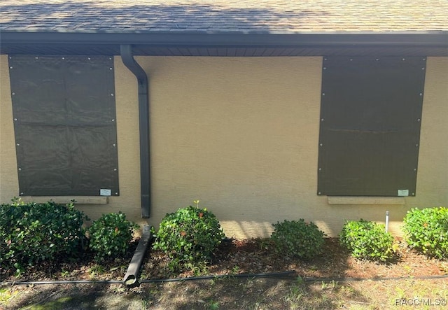 exterior space with a downspout, roof with shingles, and stucco siding