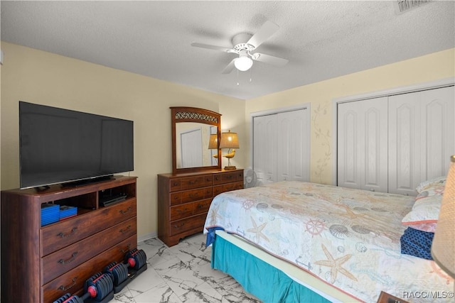 bedroom featuring a textured ceiling, ceiling fan, visible vents, marble finish floor, and two closets