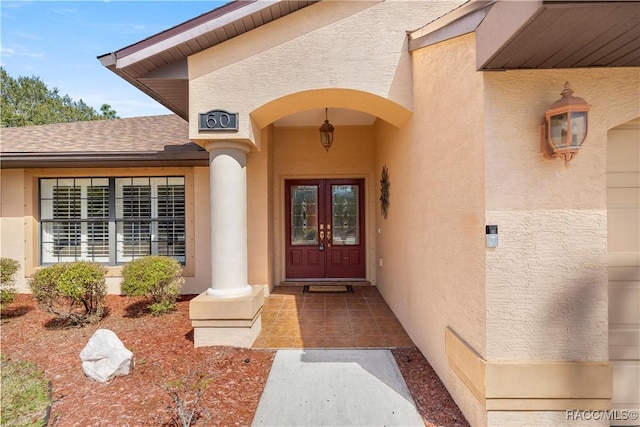 view of exterior entry with stucco siding, roof with shingles, and french doors