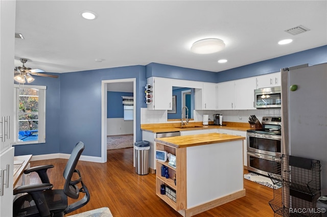 kitchen with sink, backsplash, white cabinets, butcher block counters, and stainless steel appliances