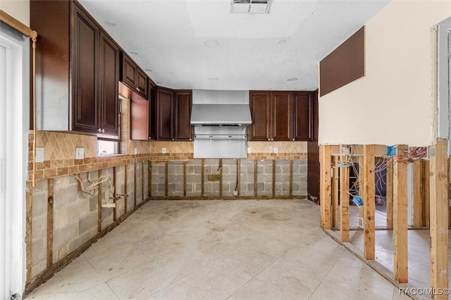 kitchen with backsplash, dark brown cabinetry, and wall chimney exhaust hood