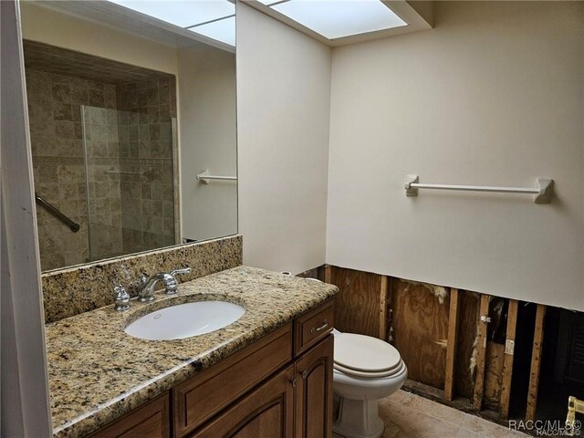 bathroom with toilet, a skylight, vanity, a tile shower, and tile patterned floors