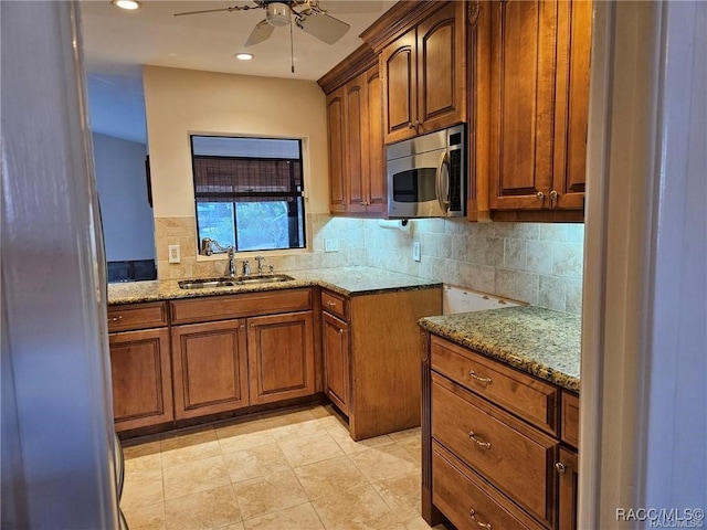 kitchen featuring light stone counters, tasteful backsplash, stainless steel microwave, a sink, and ceiling fan