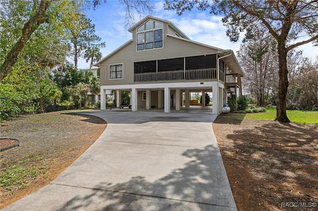 coastal home with a sunroom, stairs, a carport, and concrete driveway