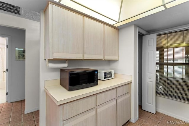 kitchen with light tile patterned floors, light countertops, visible vents, light brown cabinetry, and black microwave