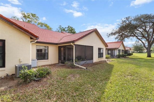 rear view of property featuring central air condition unit, a tile roof, a sunroom, a yard, and stucco siding