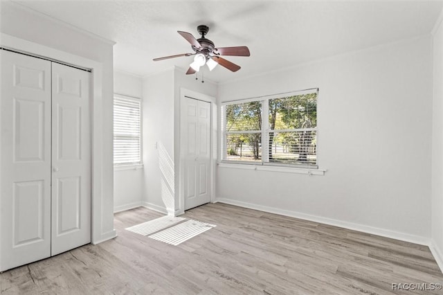 unfurnished bedroom featuring ceiling fan, light hardwood / wood-style flooring, ornamental molding, and multiple closets