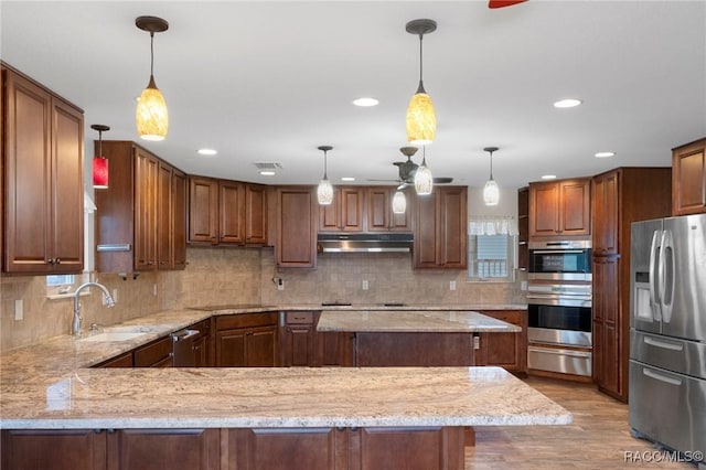 kitchen with pendant lighting, stainless steel appliances, a center island, and light stone countertops