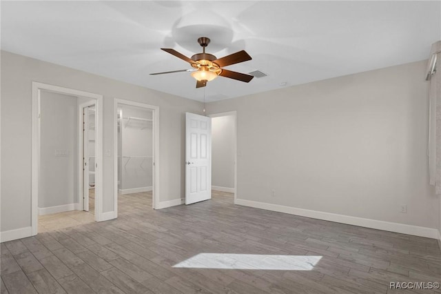 unfurnished bedroom featuring a spacious closet, a closet, ceiling fan, and light wood-type flooring