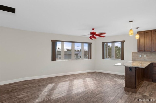 kitchen with a breakfast bar area, dark hardwood / wood-style flooring, decorative backsplash, ceiling fan, and light stone countertops