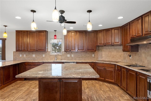 kitchen featuring light stone counters, decorative light fixtures, a kitchen island, black electric stovetop, and light hardwood / wood-style floors