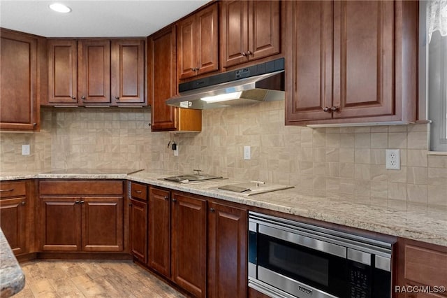 kitchen with black electric cooktop, stainless steel microwave, and light stone counters