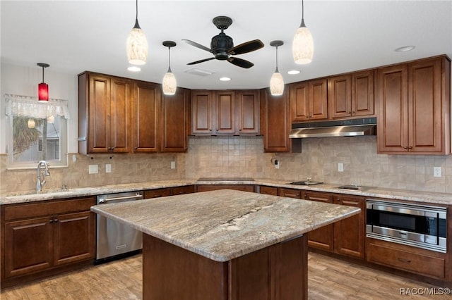 kitchen with decorative light fixtures, sink, a center island, light stone counters, and stainless steel appliances