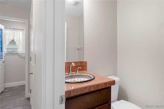 bathroom featuring vanity, toilet, hardwood / wood-style floors, and backsplash