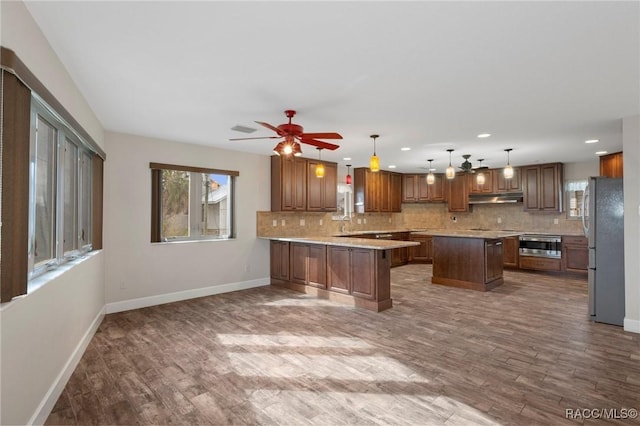 kitchen with pendant lighting, tasteful backsplash, kitchen peninsula, hardwood / wood-style flooring, and stainless steel appliances