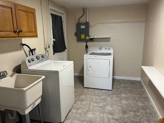 clothes washing area with washer and dryer, cabinets, sink, and electric panel