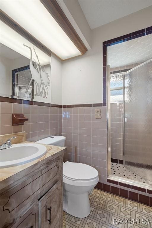 bathroom with tile walls, vanity, toilet, and a shower with shower door