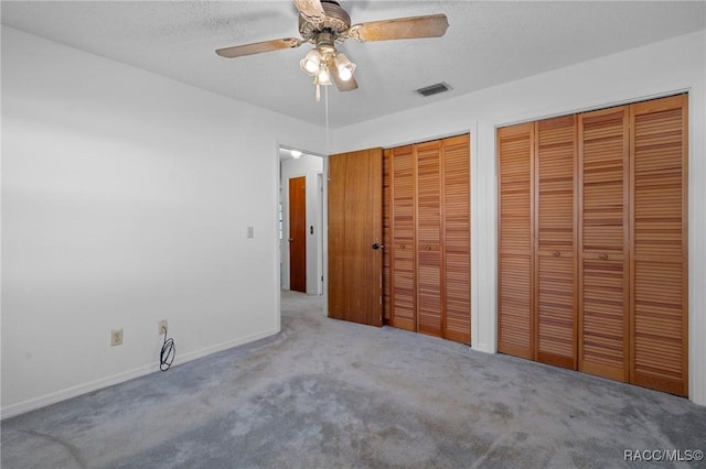 unfurnished bedroom with carpet, ceiling fan, a textured ceiling, and two closets