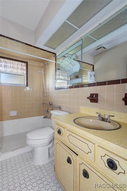 bathroom featuring toilet, tile walls, backsplash, and vanity