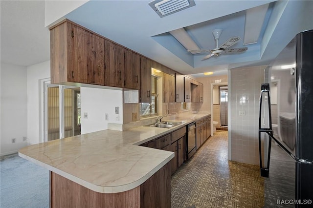 kitchen with sink, black fridge, stainless steel dishwasher, kitchen peninsula, and a raised ceiling