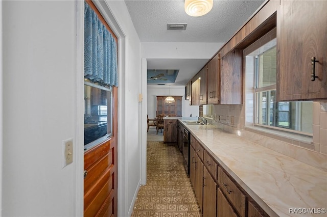 kitchen with hanging light fixtures, black dishwasher, sink, a textured ceiling, and decorative backsplash