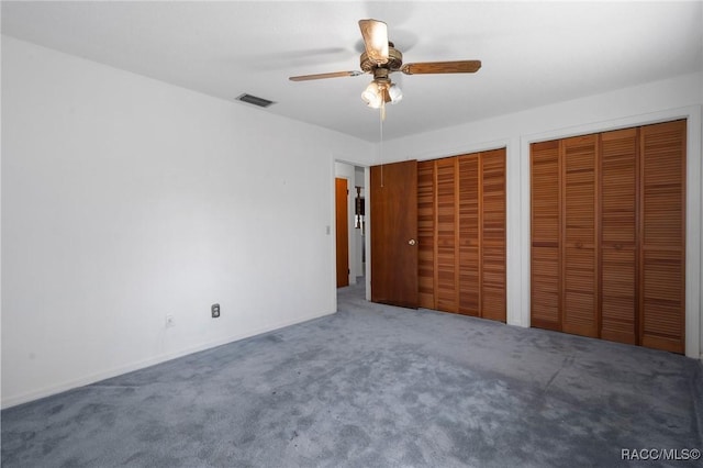 unfurnished bedroom featuring dark carpet, two closets, and ceiling fan