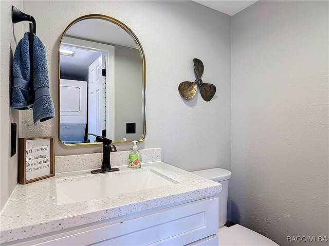 bathroom featuring vanity, stacked washer / drying machine, and toilet