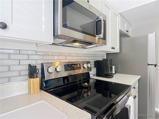 kitchen with appliances with stainless steel finishes, white cabinets, backsplash, and light stone counters