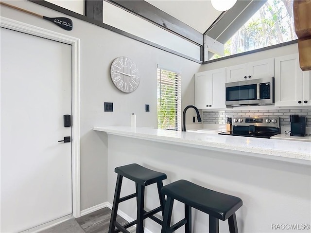 kitchen with white cabinets, appliances with stainless steel finishes, decorative backsplash, and a breakfast bar area