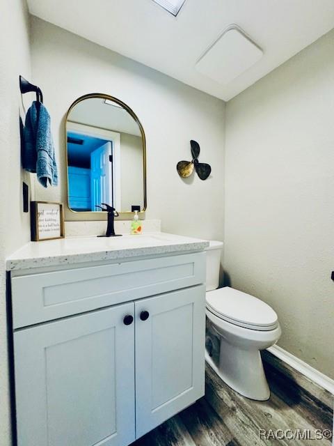 bathroom with baseboards, wood finished floors, toilet, and vanity