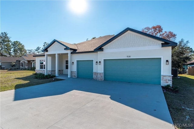 view of front of property featuring central air condition unit, concrete driveway, a front yard, a garage, and stone siding