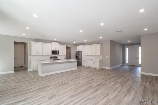 kitchen featuring appliances with stainless steel finishes, an island with sink, sink, white cabinets, and light wood-type flooring