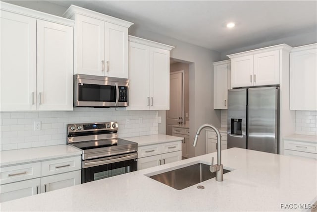 kitchen featuring appliances with stainless steel finishes, a sink, white cabinetry, and tasteful backsplash