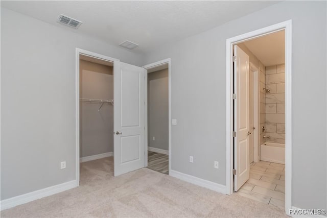 unfurnished bedroom featuring ensuite bathroom, a spacious closet, light carpet, and a closet