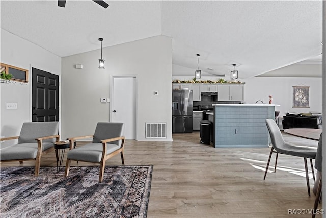 living room featuring a textured ceiling, light hardwood / wood-style floors, ceiling fan, and lofted ceiling