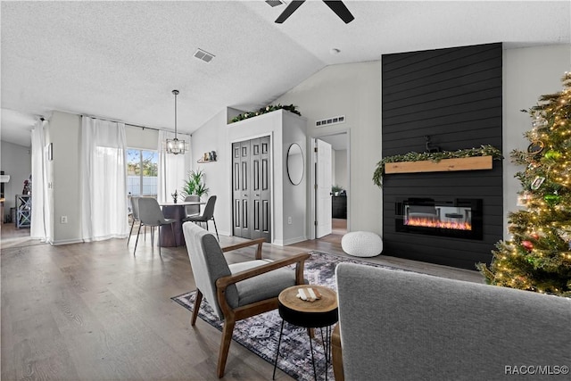 living room featuring ceiling fan with notable chandelier, a textured ceiling, a large fireplace, vaulted ceiling, and hardwood / wood-style flooring